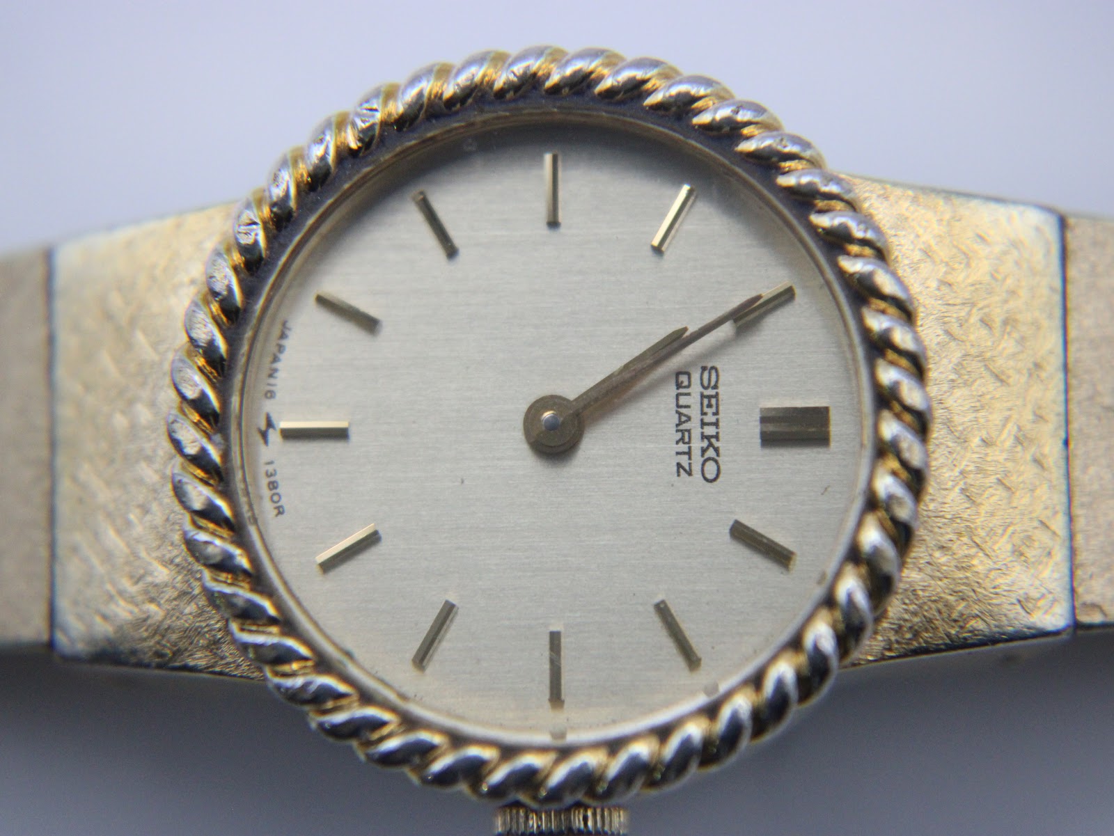 Extreme close-up of the watch dial, showcasing the gold brushed finish, applied gold baton indices, and twisted rope bezel.