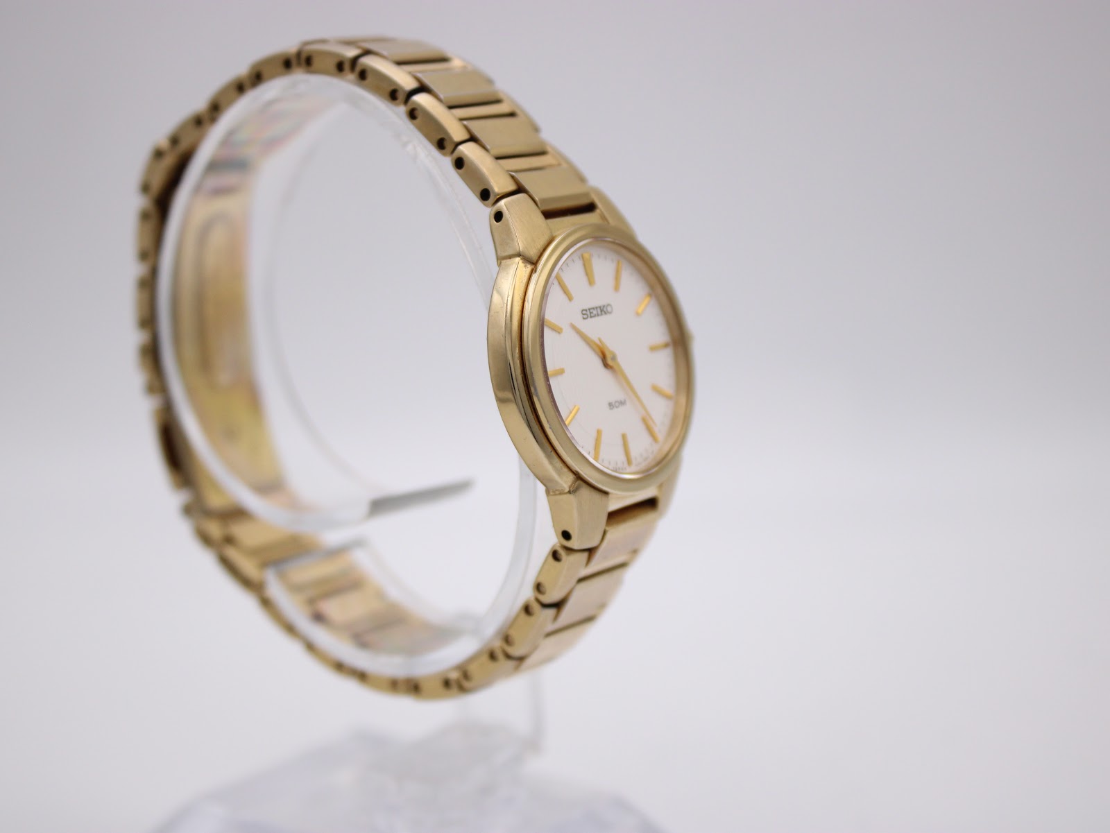 Another angled side view of the gold tone Seiko watch, showing the integrated bracelet design on a clear stand.