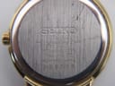 Close-up of the brushed stainless steel case back of the Seiko watch, showing model number, serial, and "sapphire crystal" engraving.