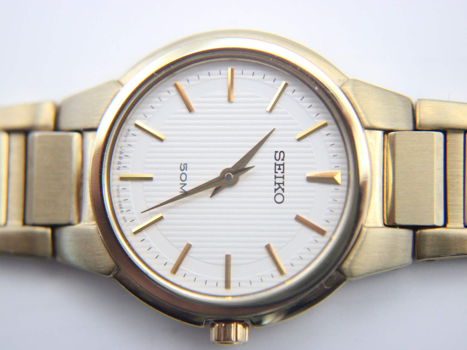 Macro close-up of the white dial of the Seiko watch, showing gold baton indices, textured surface, and "50M" text.