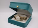 The gold tone Seiko watch displayed inside a teal coloured gift box with a small golden crown decoration on the lid.