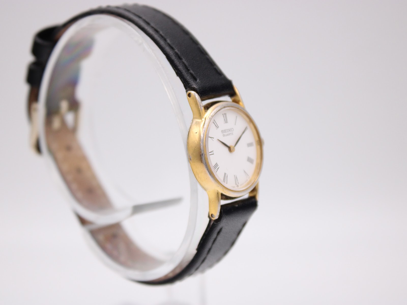 Another angled side view of the Seiko watch, showing the case profile and black leather strap on a stand.