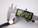 Digital caliper measuring the watch case diameter at 20.23mm, with the watch face visible on a white background.