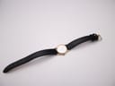 Overhead view of the small gold tone Seiko watch with its black leather strap laid flat on a white surface.
