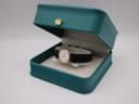The Seiko watch with its black leather strap displayed within an open teal coloured presentation box with a gold crown emblem.