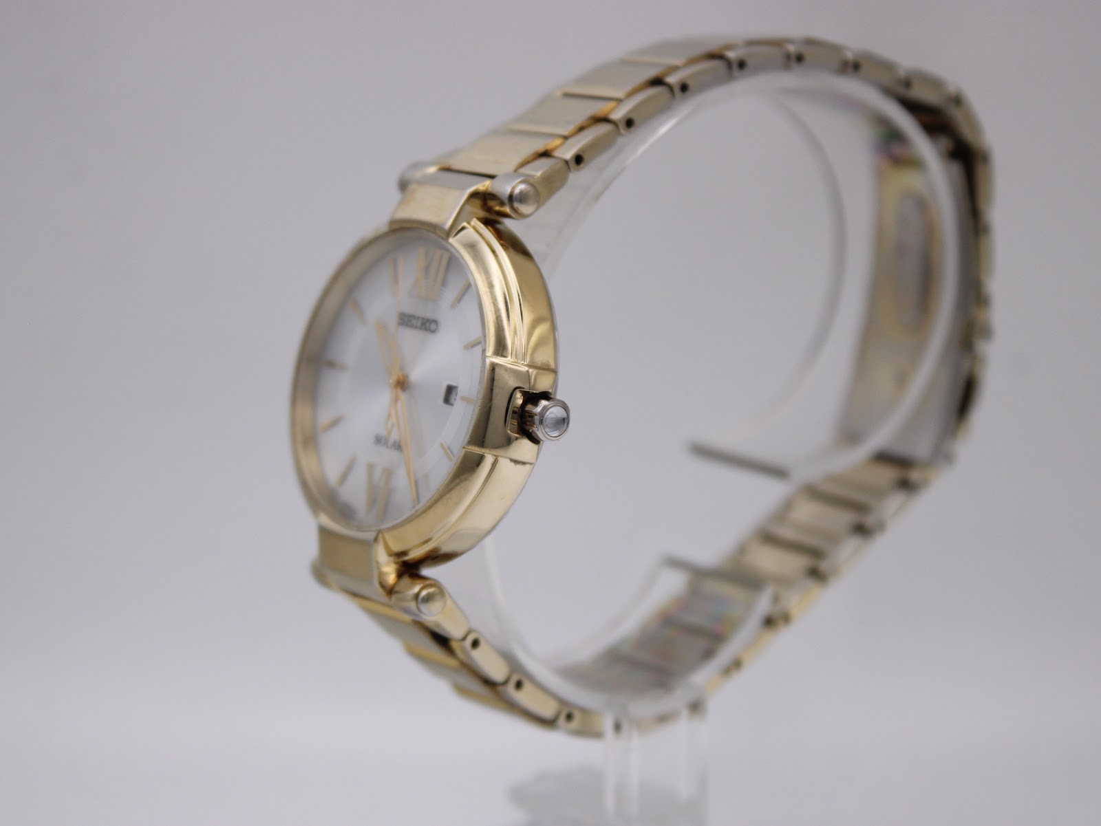 Side profile view showing the elegant gold tone watch case, crown, and integrated steel bracelet.