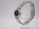 Angled side view of the Seiko watch, showing the silver-tone case and integrated bracelet on a clear display stand.