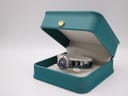 The Seiko watch resting in a teal-coloured presentation box with a gold crown emblem.