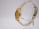 Angled side view of the gold Seiko watch showing the crown and case profile on a transparent display stand.