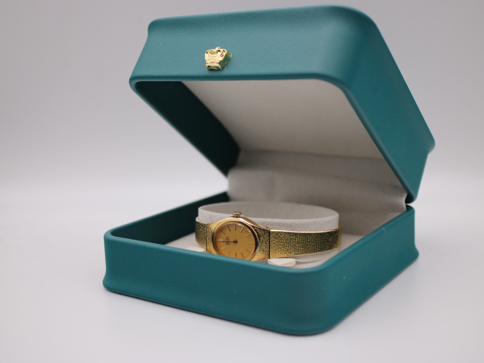 The gold Seiko watch displayed in an open teal presentation box, resting on a beige cushion.
