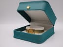 The gold Seiko watch displayed in an open teal presentation box, resting on a beige cushion.