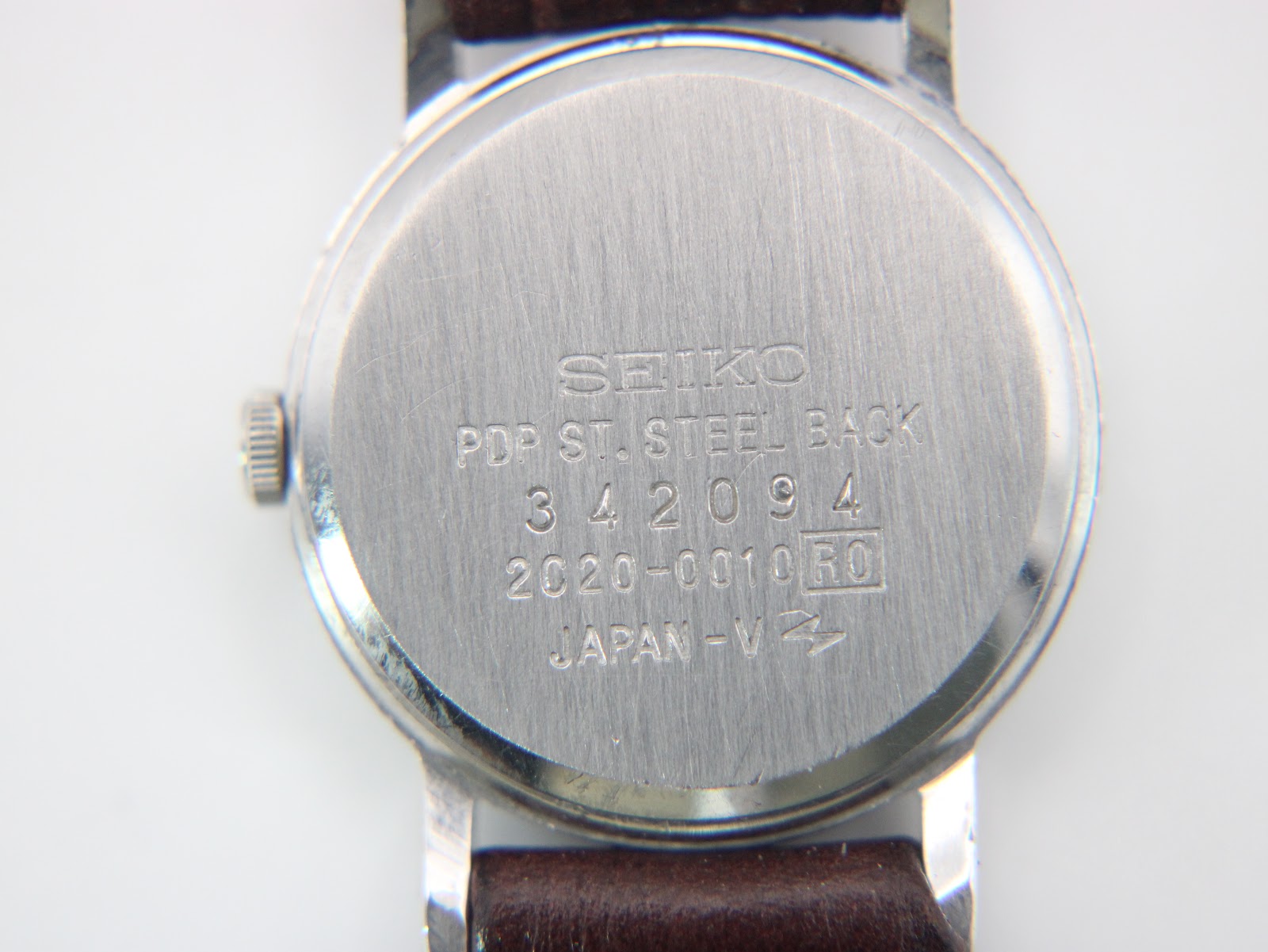 Detail of the dark brown textured leather strap and unbranded buckle.