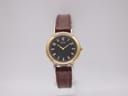 Front view of Seiko 1N00-0A10 watch with black dial and gold case on a display stand.
