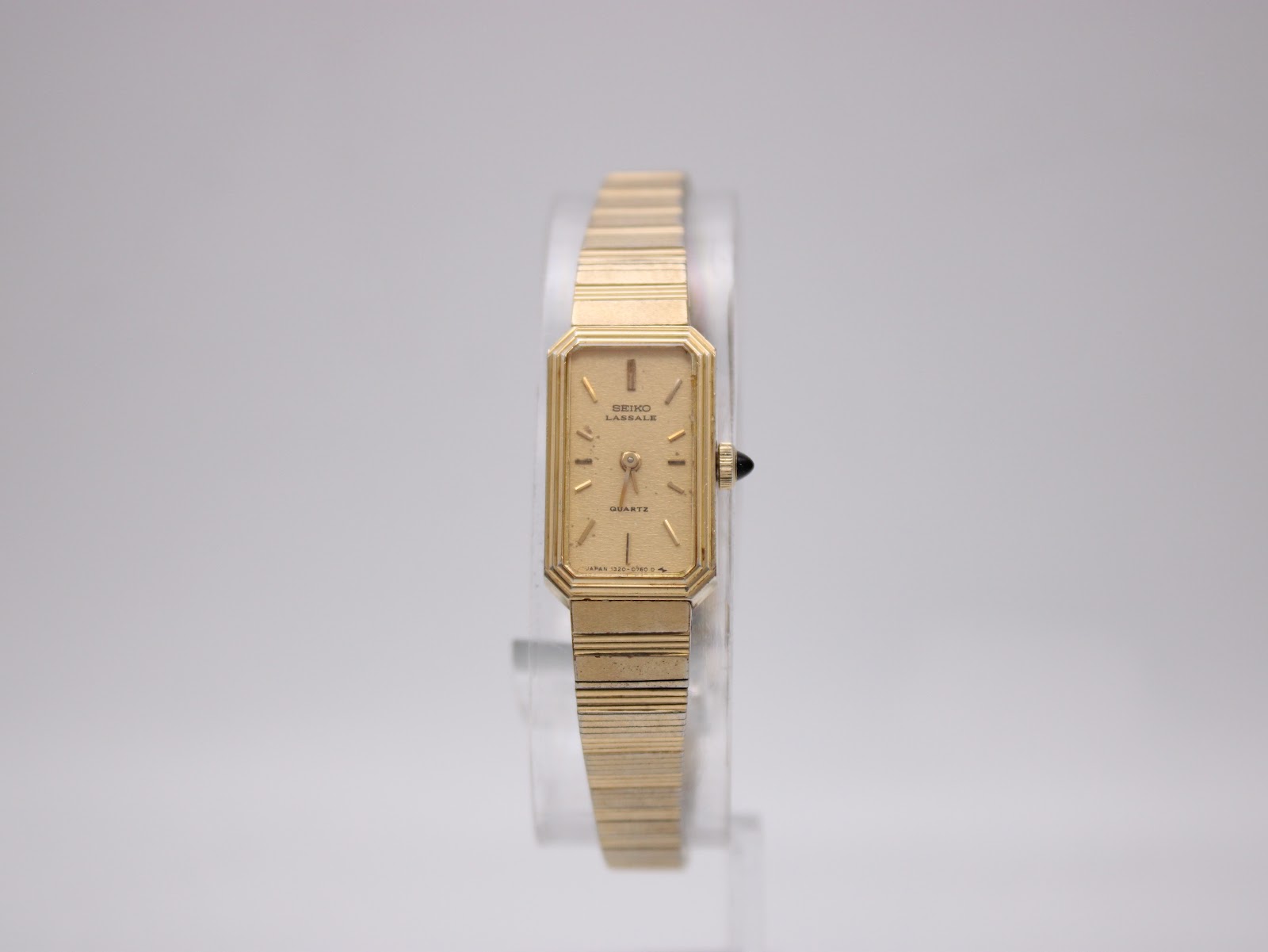 Front view of the Seiko Lassale gold-tone rectangular quartz watch on a clear display stand, showing the dial and bracelet.