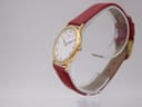 Three-quarter side view of the Seiko watch, showing the profile of the gold-tone case, the crown, and the texture of the burgundy strap on a clear stand.
