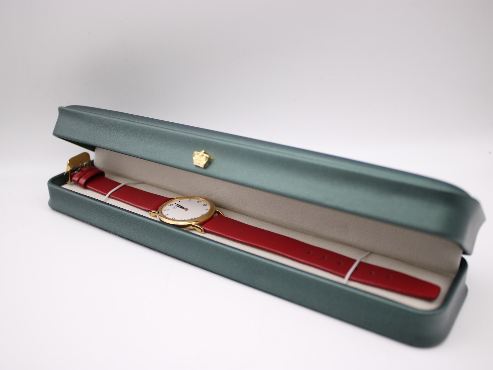 The Seiko watch with burgundy strap resting inside a green presentation box.