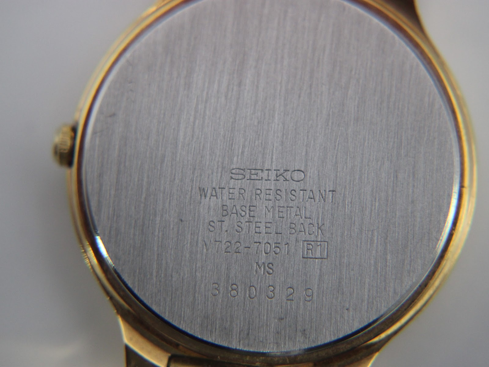 Detailed close-up of the brushed stainless steel case back with Seiko branding, model number V722-7051, and serial number 380329.