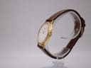 Side profile view of the slim gold-plated Seiko quartz watch on a clear stand.