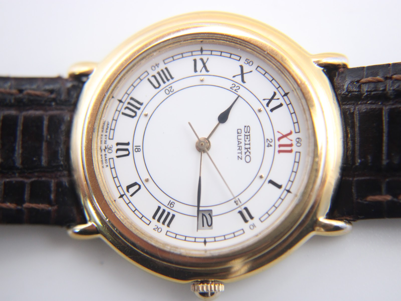 Detailed close-up of the white dial with black Roman numerals, red 'XII', inner 24-hour track, and date window.