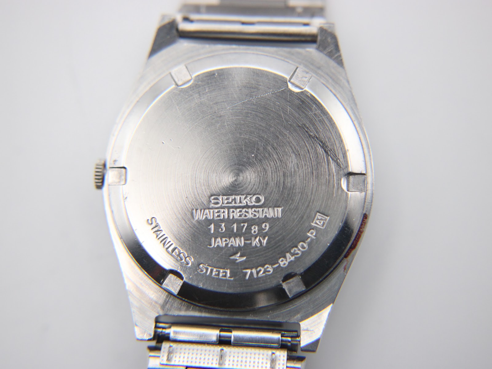Close-up of the stainless steel case back of the Seiko watch, displaying engravings including 'SEIKO', 'WATER RESISTANT', serial number '131789', 'JAPAN-KY', and model number '7123-8430-P'.