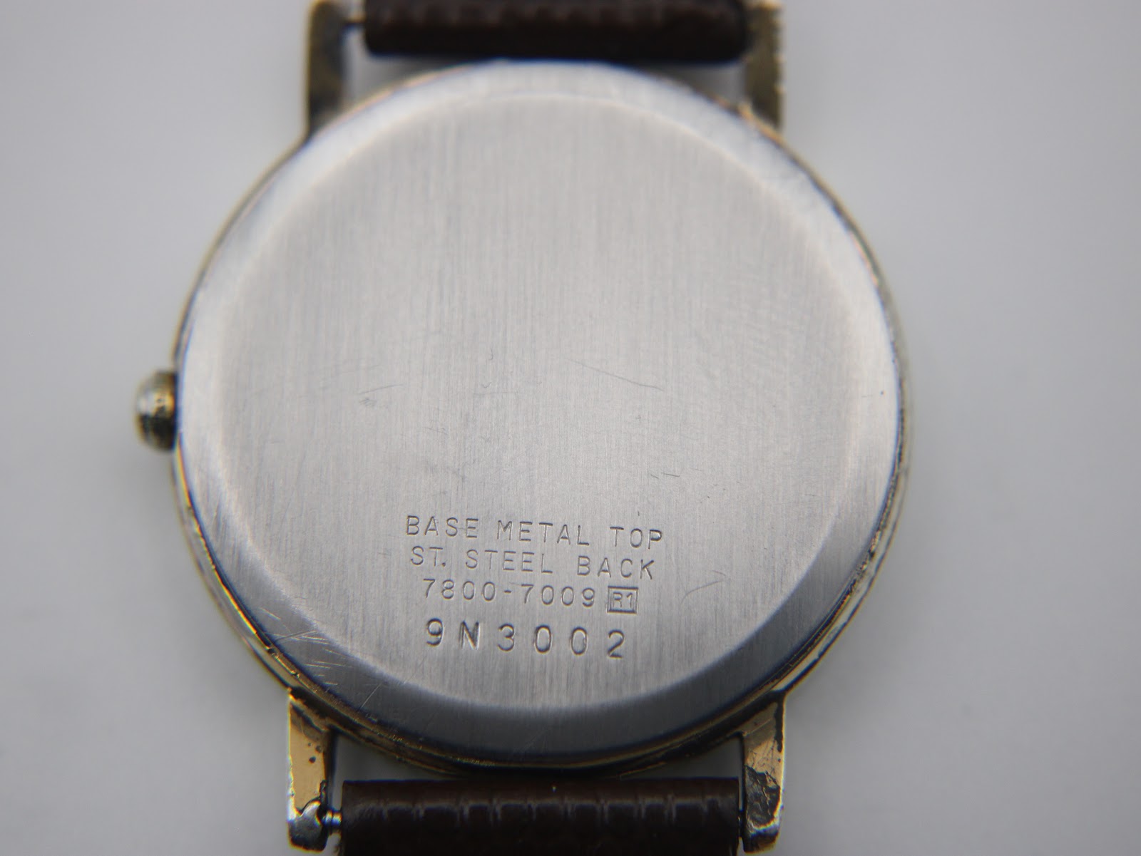 Close-up of the watch's stainless steel case back, engraved with "BASE METAL TOP", "ST. STEEL BACK", "7800-7009", and serial "9N3002".