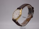 Angled view of the Seiko watch, showing the gold tone case, white dial, and brown leather strap on a watch stand.