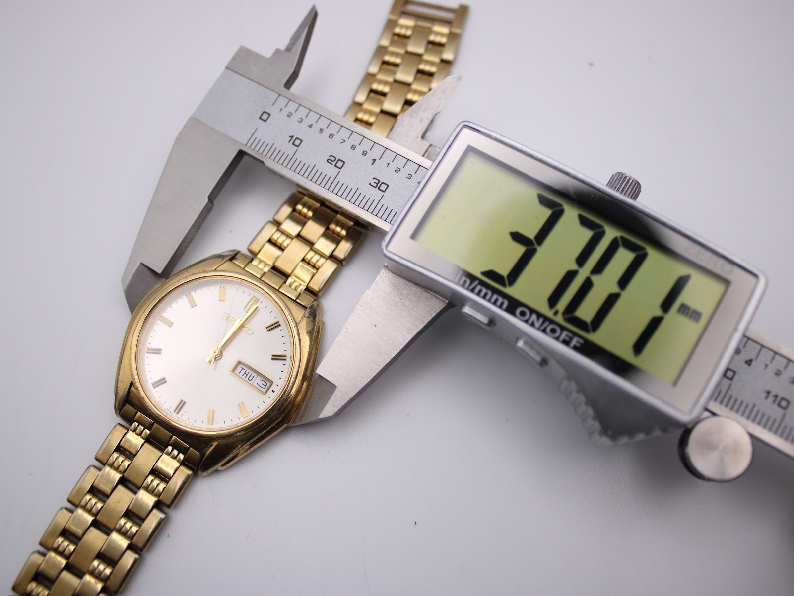 Digital caliper measuring the case diameter of the Seiko watch, showing a precise reading of 37.01mm.