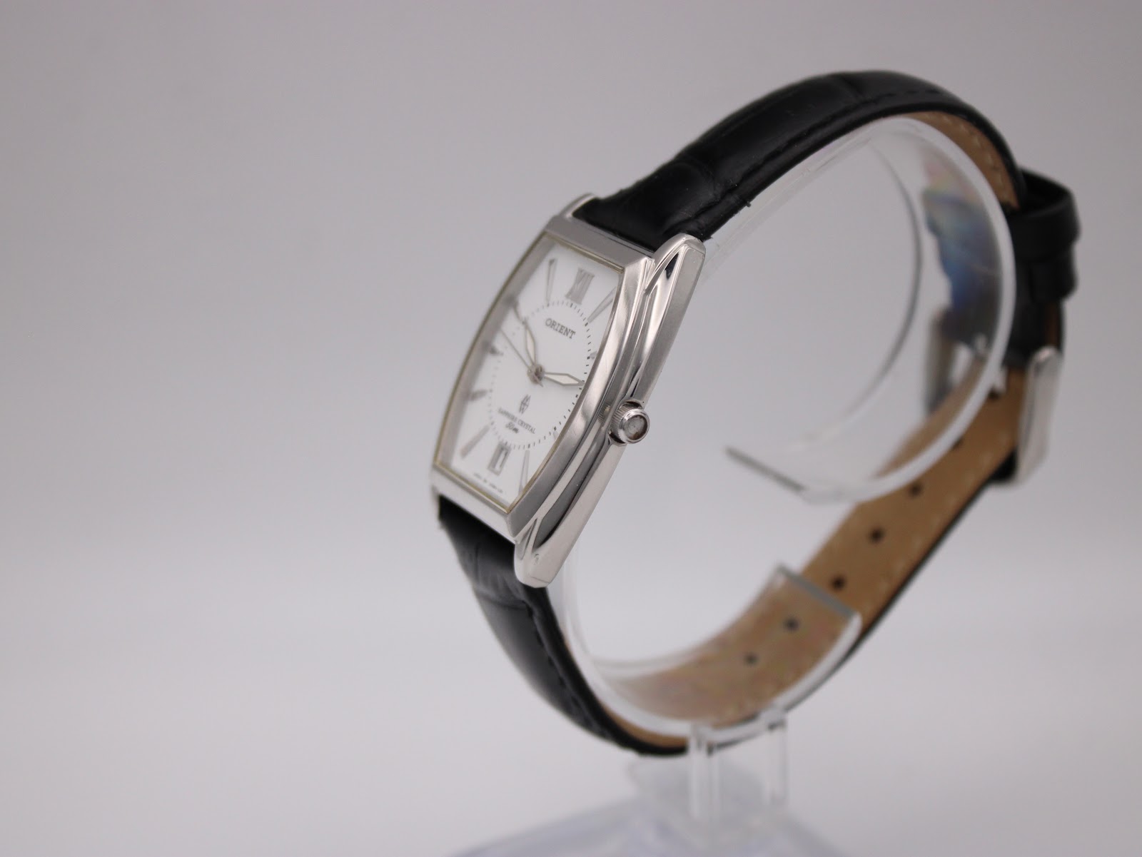 Side view of the Orient UNBH-CO watch on a stand, showing the curved profile of the polished silver-tone case and the black leather strap.