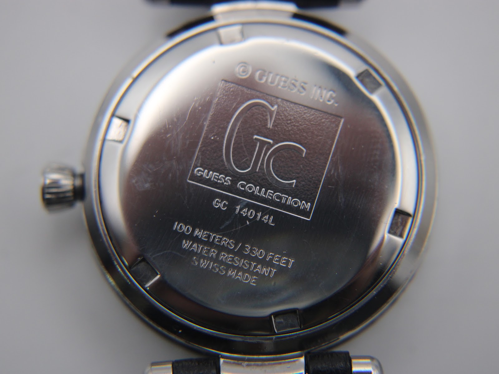 Close-up of the polished stainless steel case back with "Gc Guess Collection 14014L" and "100 metres / 330 feet Water Resistant Swiss Made" engravings.