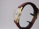 Side profile view of the gold plated Seiko watch on a display stand, showing the crown and domed acrylic crystal.
