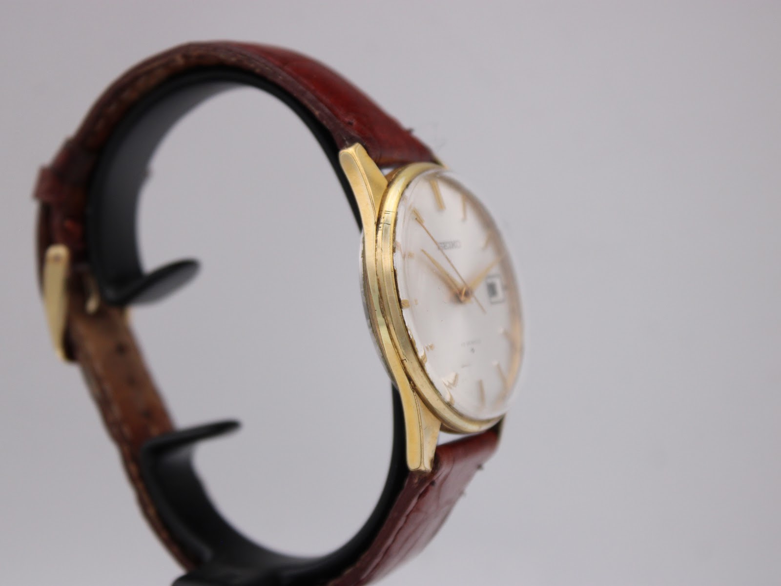 Opposite side profile view of the gold plated Seiko watch on a display stand, showing the curved lugs.