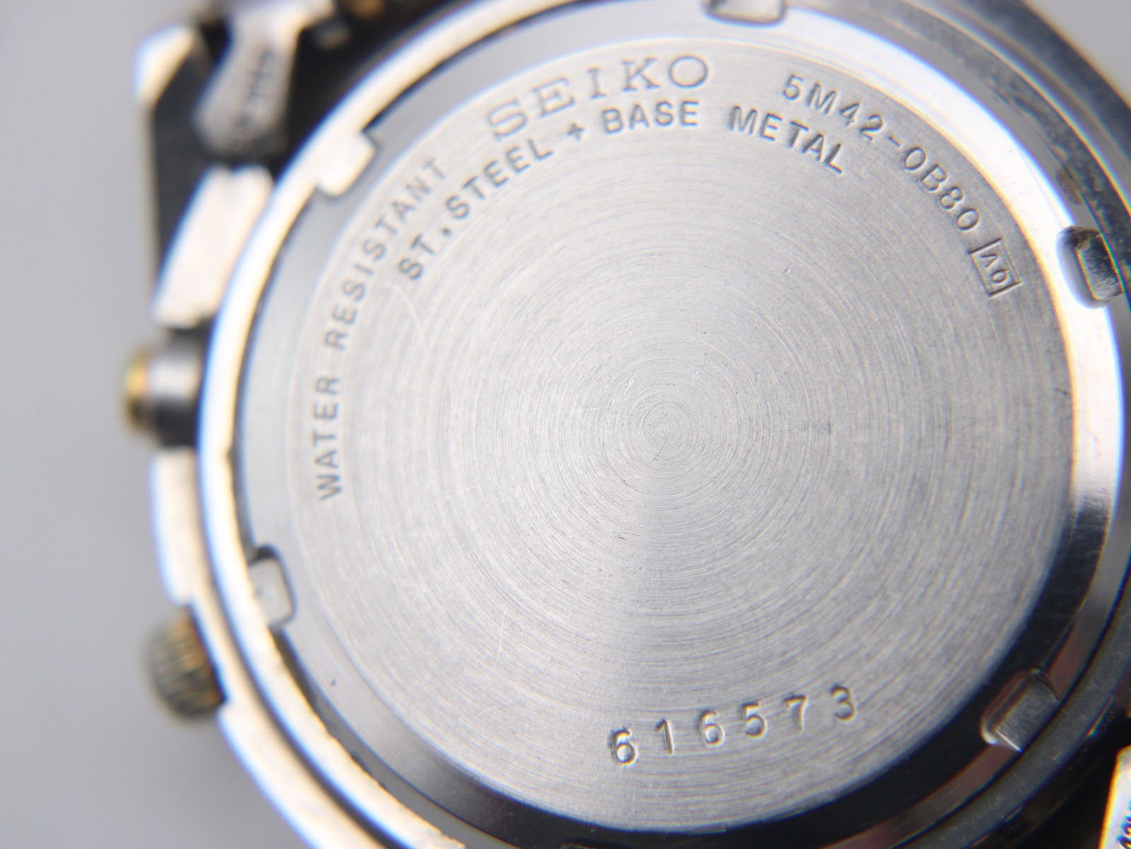 Close-up of the Seiko watch's stainless steel case back, showing "SEIKO", "5M42-0B80", "WATER RESISTANT", and serial number "616573".
