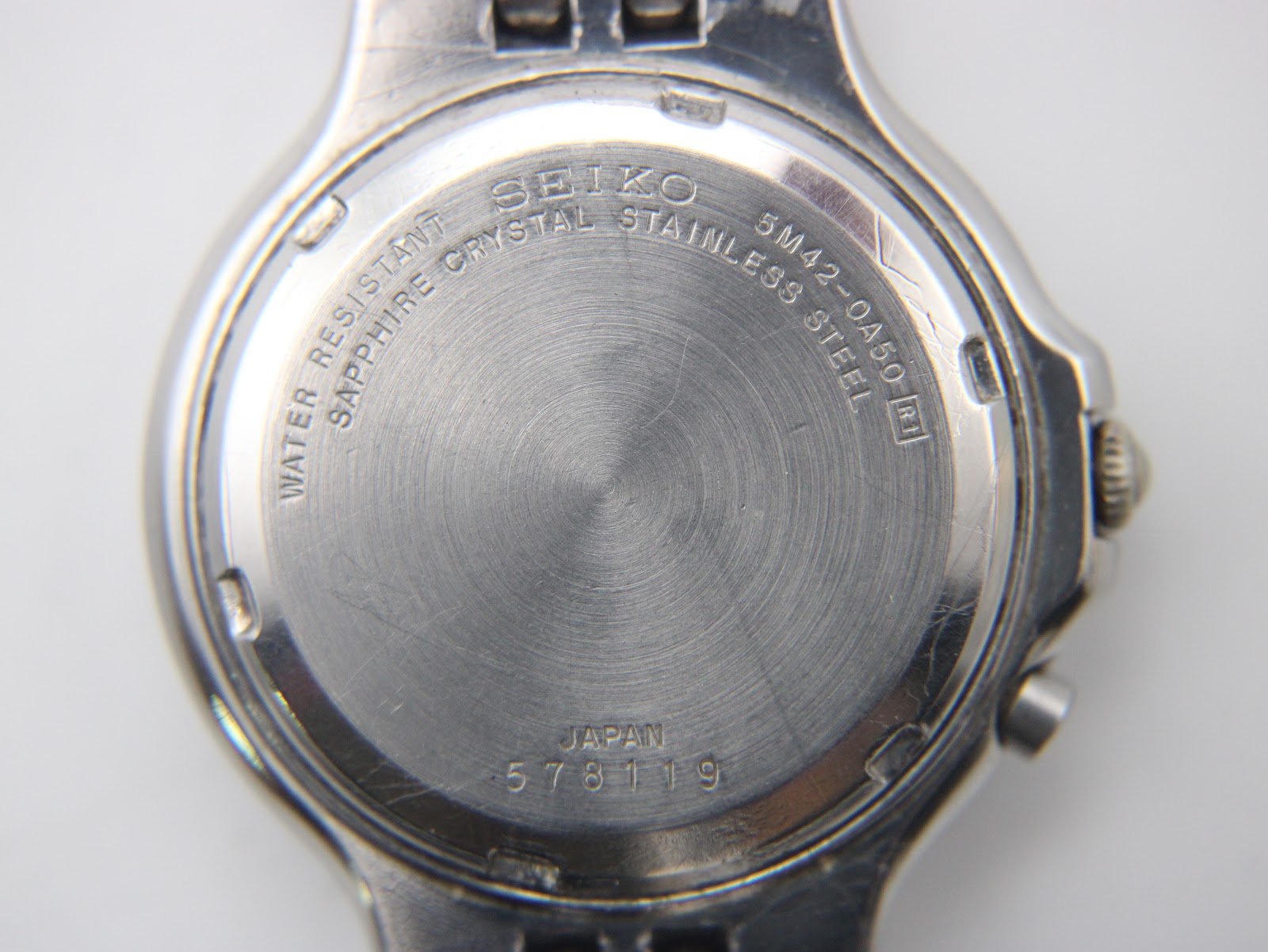 Close-up of the watch case back, showing "SEIKO 5M42-0A50 WATER RESISTANT SAPPHIRE CRYSTAL STAINLESS STEEL JAPAN 578119".