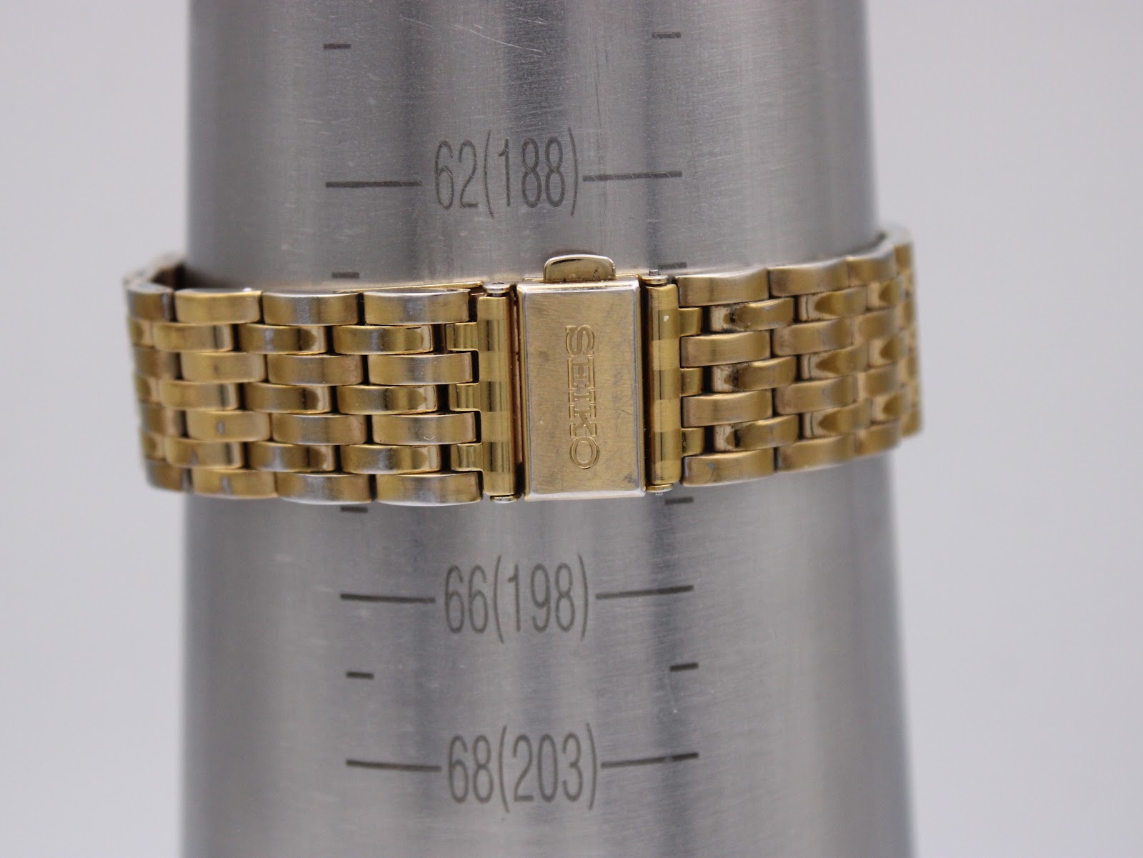 Close-up of the gold-tone steel bracelet and signed Seiko clasp on a wrist sizing gauge, showing a wrist circumference of 198mm.