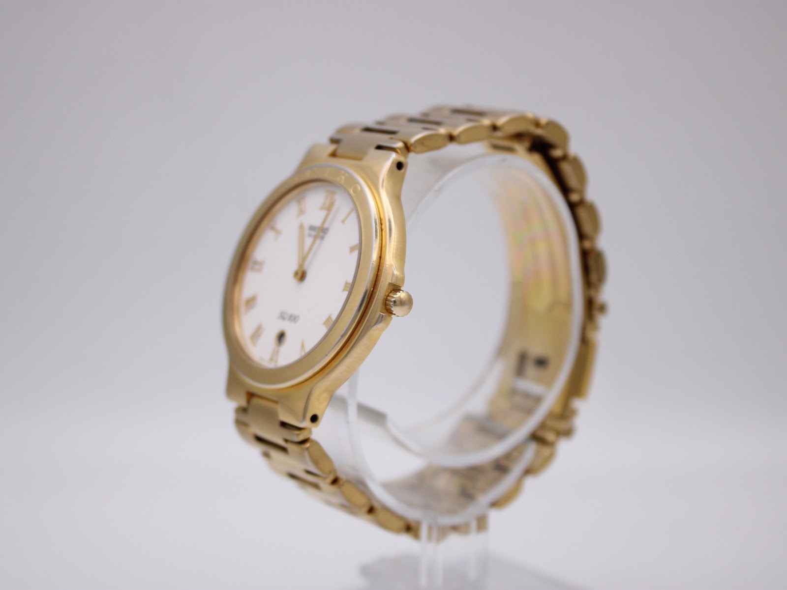 Angled view of the Seiko SQ100 watch, showcasing the gold-toned case and integrated bracelet on a clear stand.
