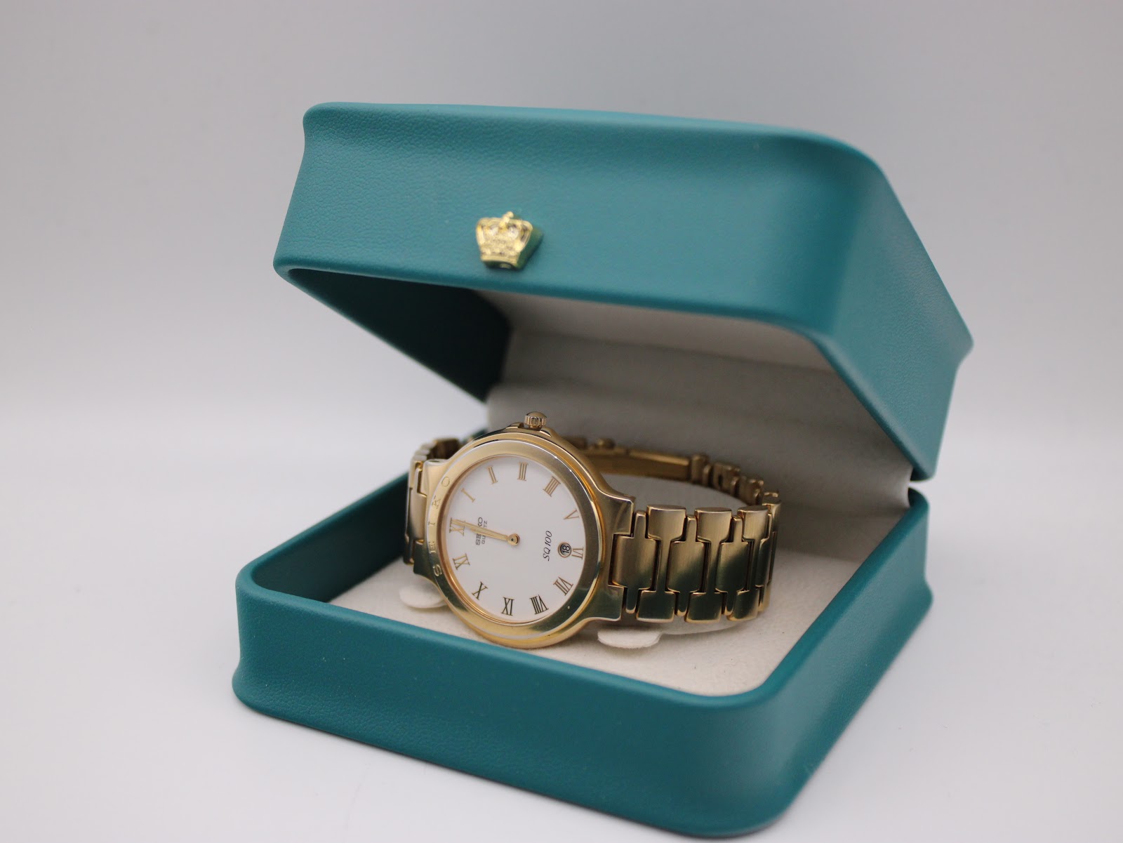 The Seiko SQ100 watch resting in an open turquoise display box with a gold crown emblem, used for presentation.