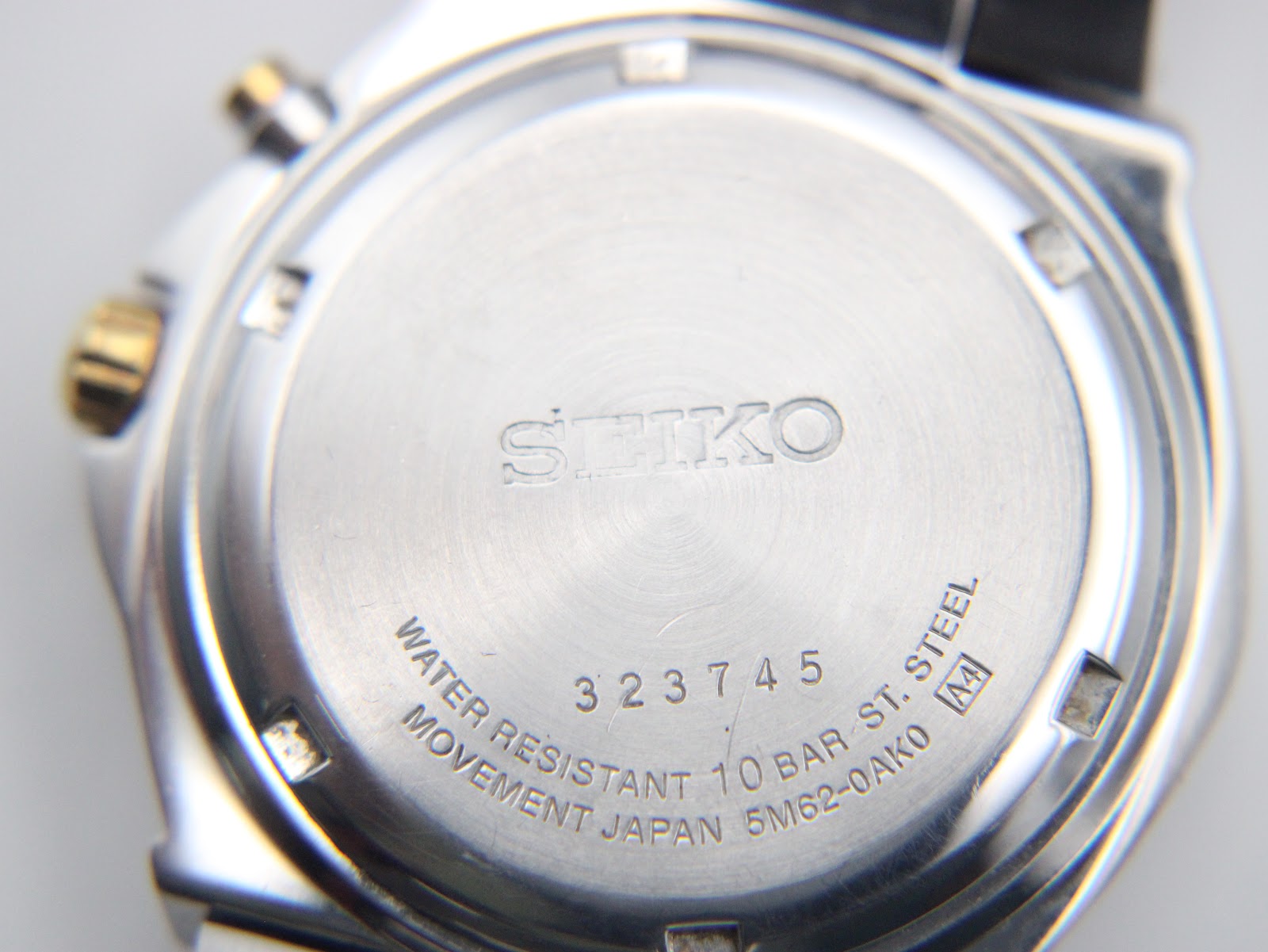 Close-up of the watch case back showing Seiko branding, serial number 323745, model 5M62-0AK0, and 10 BAR water resistance.
