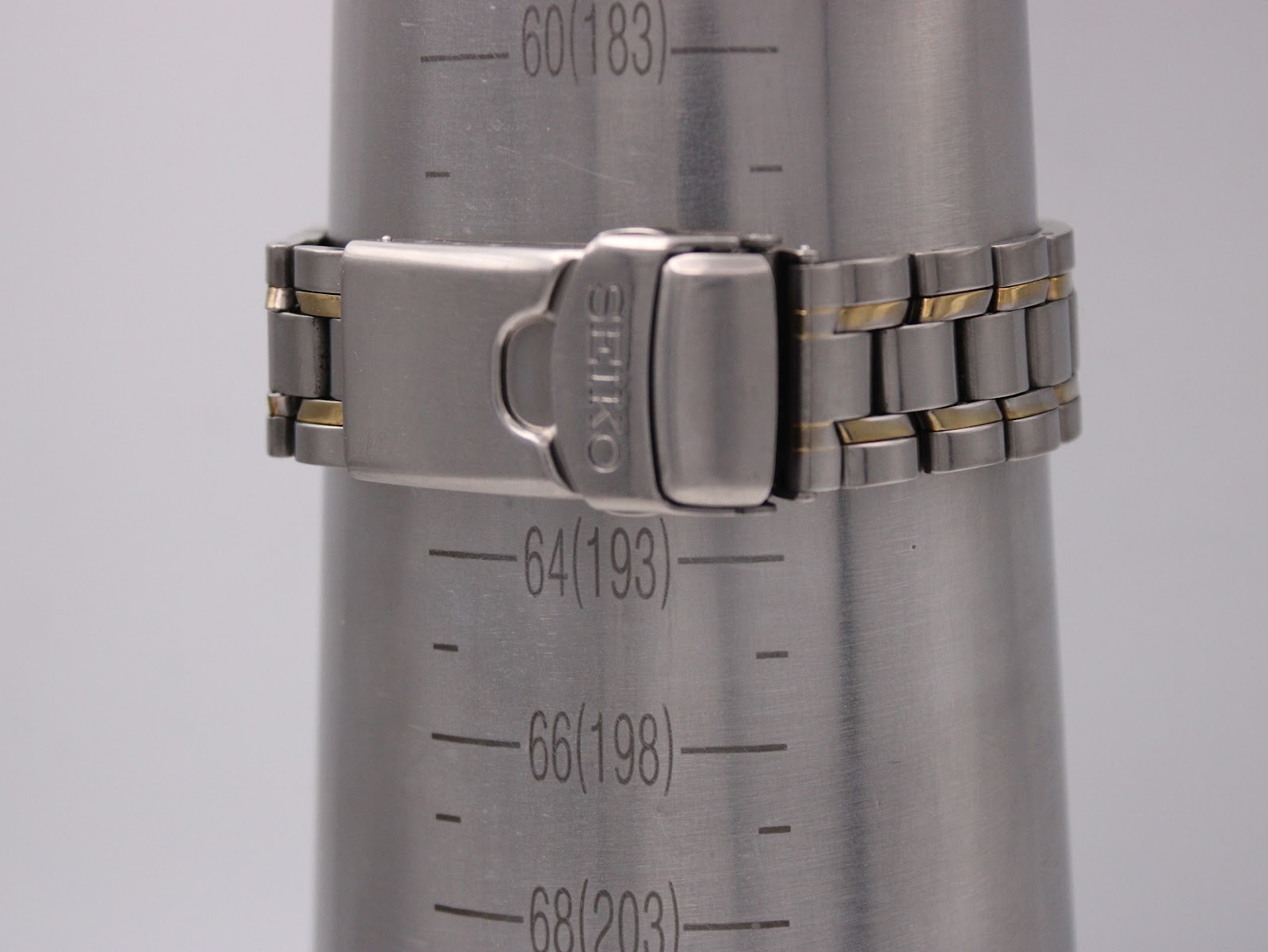 The signed Seiko two-tone deployant clasp of the bracelet, resting on a wrist sizing cone at 6.0 inches / 18.3 cm.