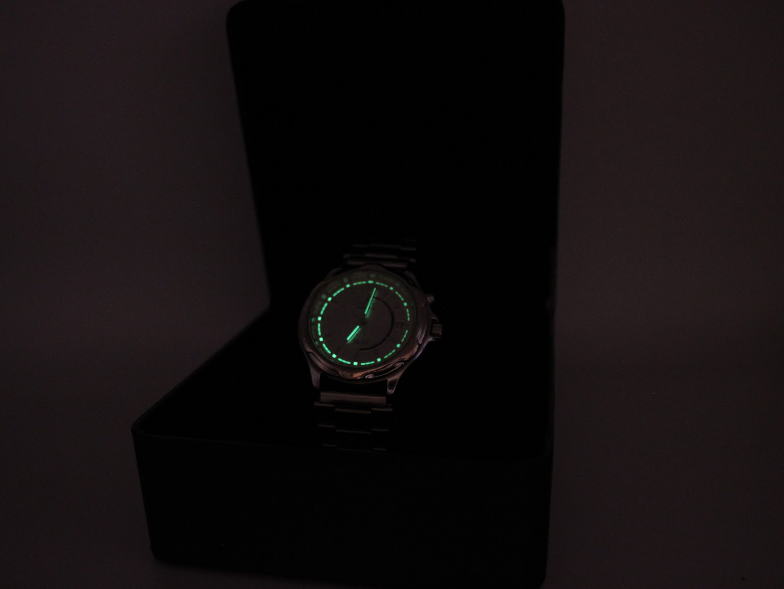 Low light view of the Seiko watch dial showcasing the bright green luminescence on the hands and hour markers.