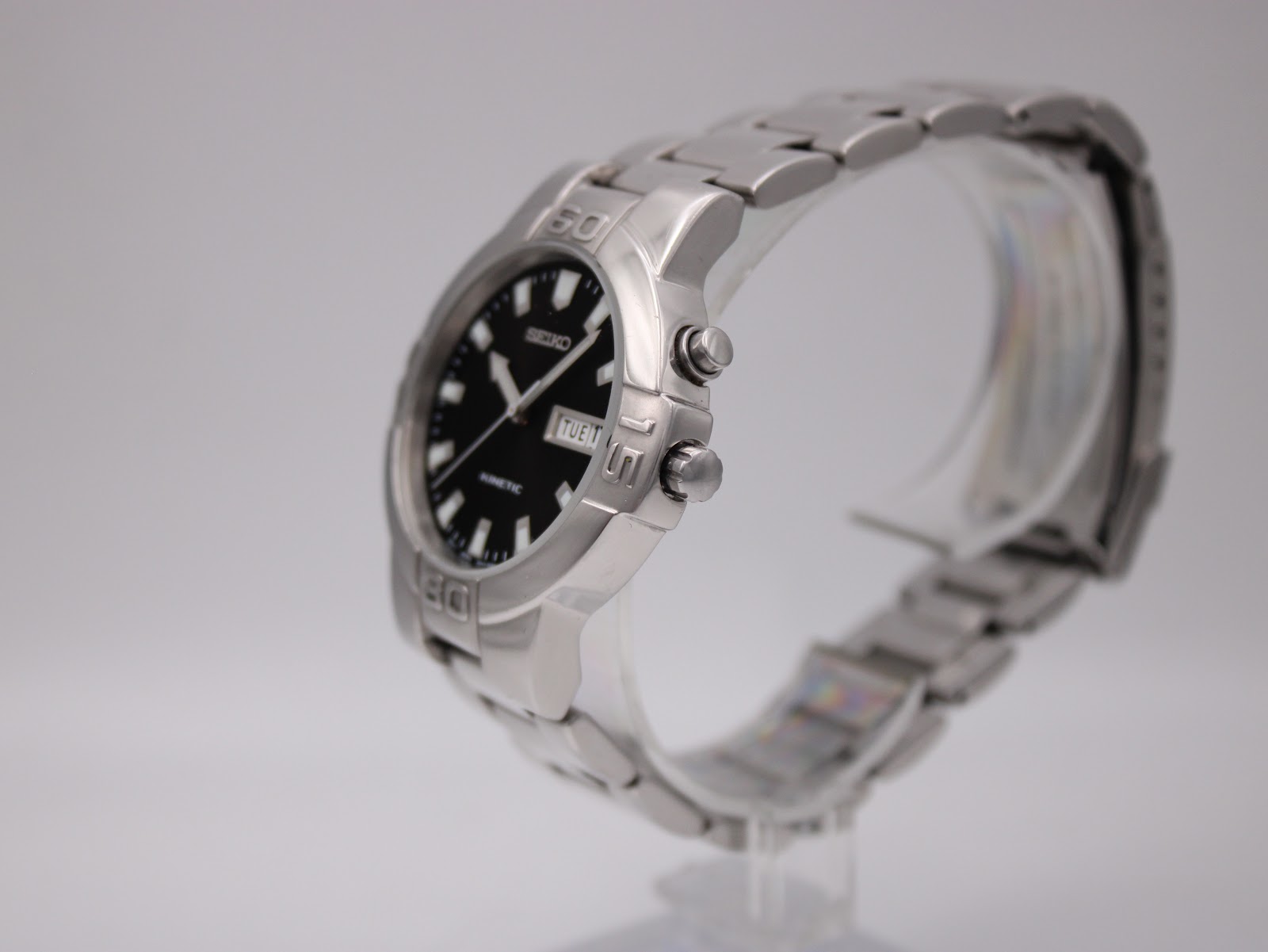 Angled right side view of the Seiko kinetic watch on a display stand, showing the crown and push-button.