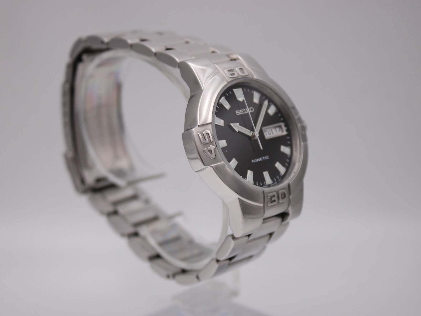 Angled left side view of the Seiko kinetic watch on a display stand, highlighting the unique case shape and bracelet.