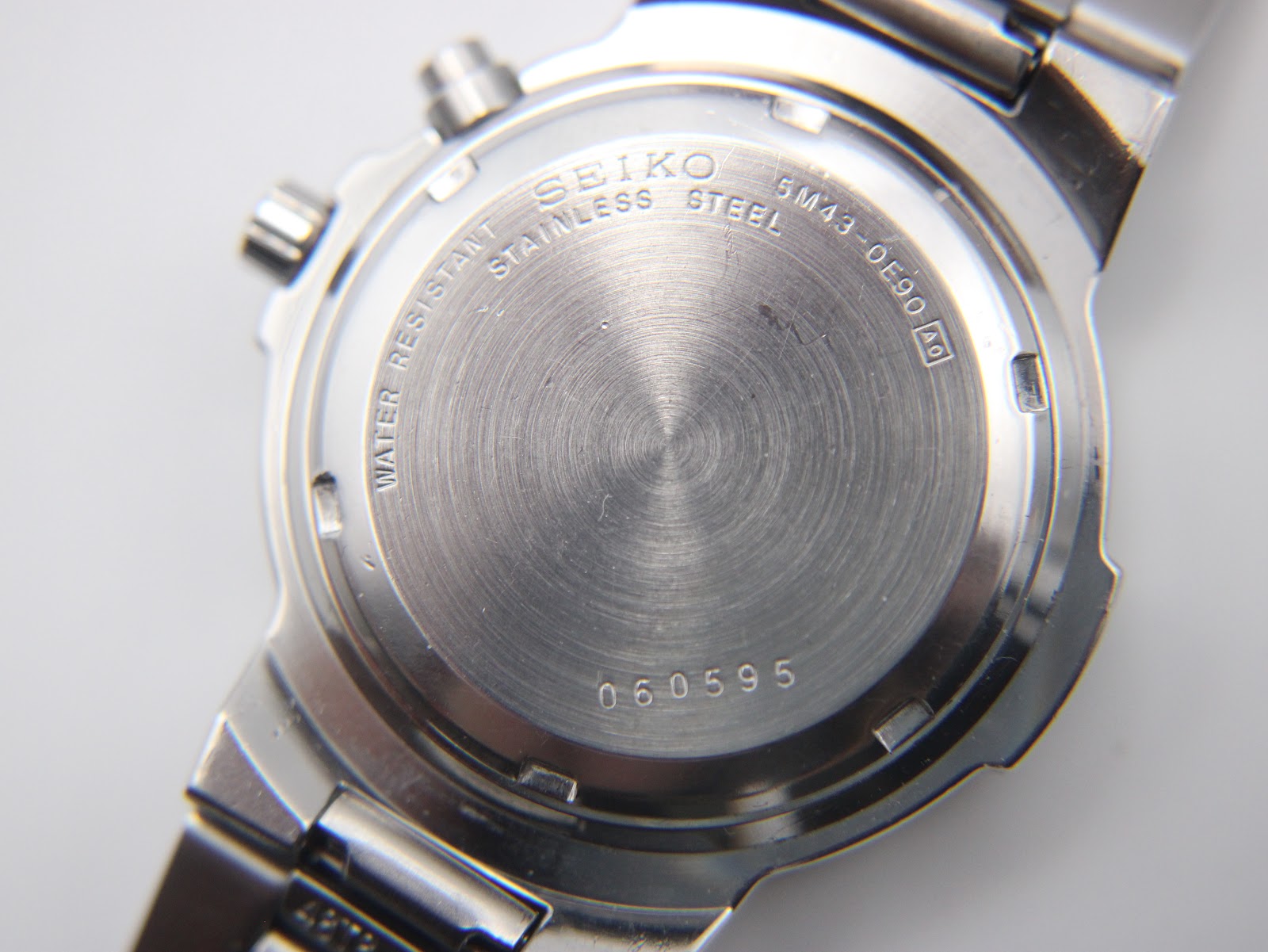 Close-up of the watch case back, showing 'SEIKO STAINLESS STEEL 5M43-0E90 A0 WATER RESISTANT' and serial number '060595'.