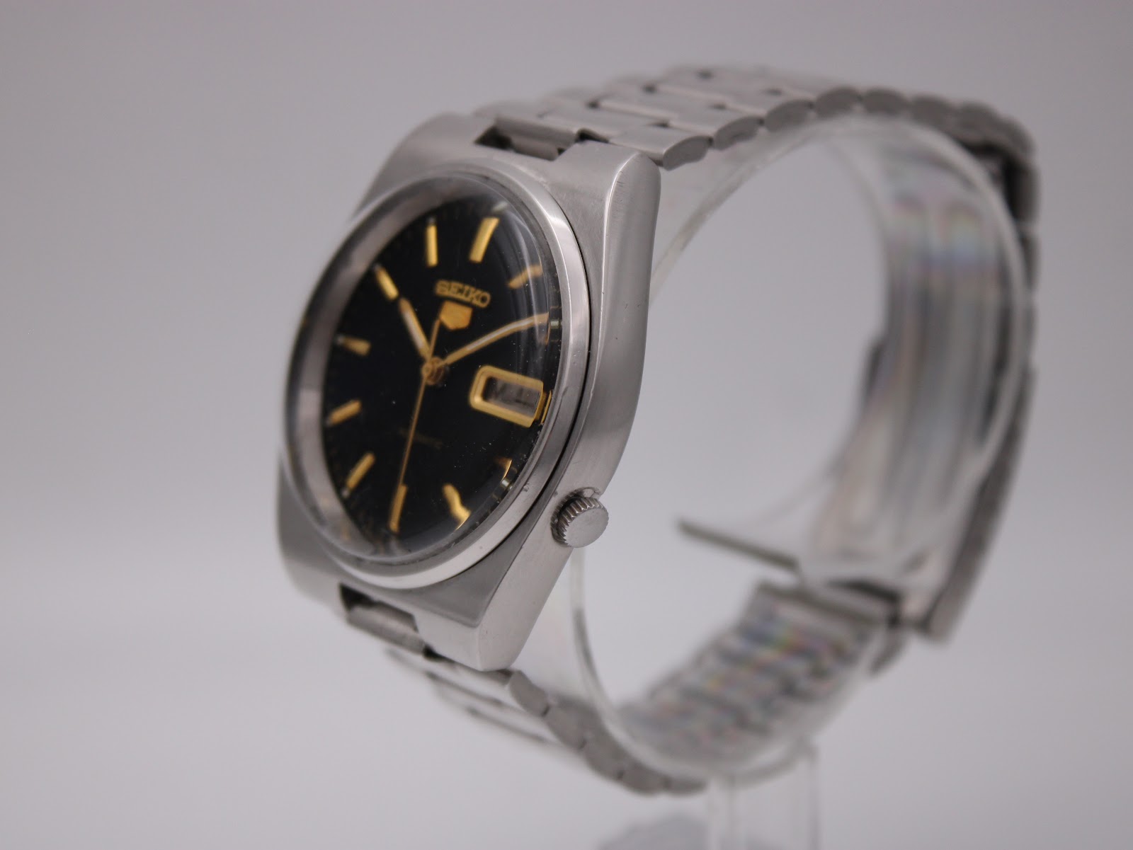 Angled side view of the Seiko 7009-3130 watch showing the stainless steel case and bracelet on a display stand.