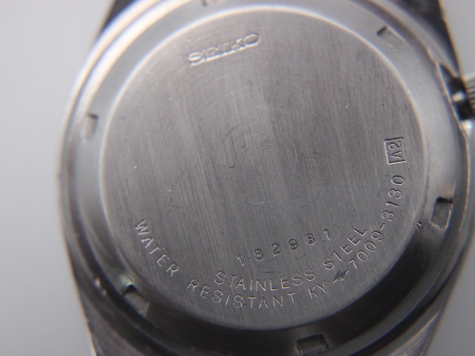 Close-up of the brushed stainless steel case back with "SEIKO", "WATER RESISTANT", "STAINLESS STEEL", "182981", and model number "7009-3130" engravings.