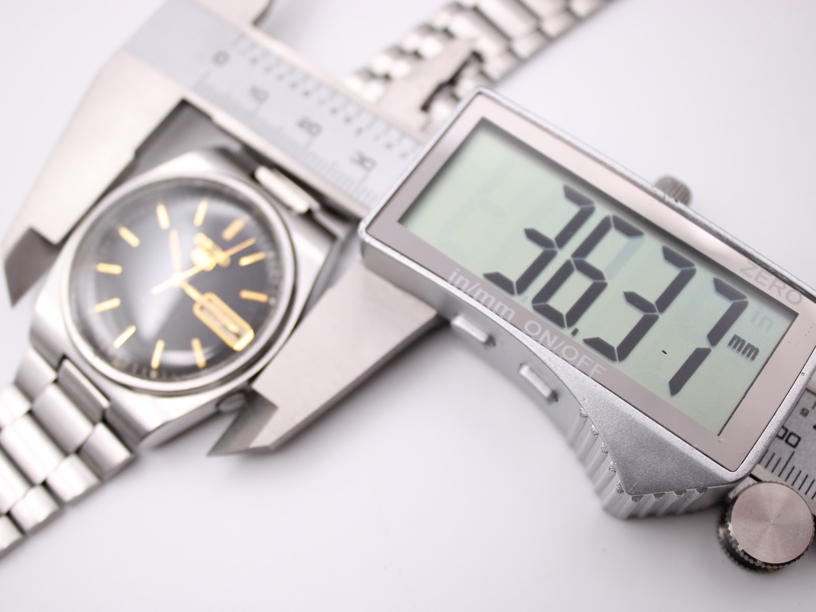 Digital caliper measuring the watch case, displaying a precise diameter of 36.37mm, with the black dial visible in the background.