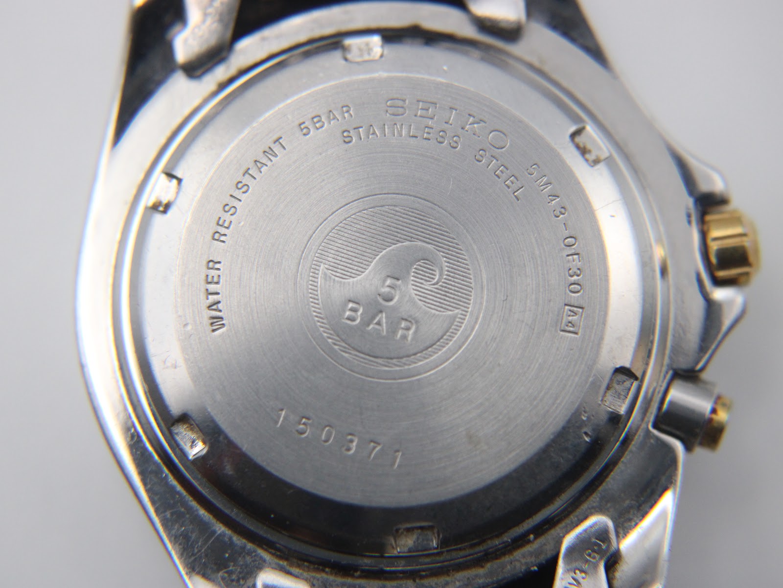 Close-up of the watch case back showing model number, serial number, and 5 BAR water resistance.