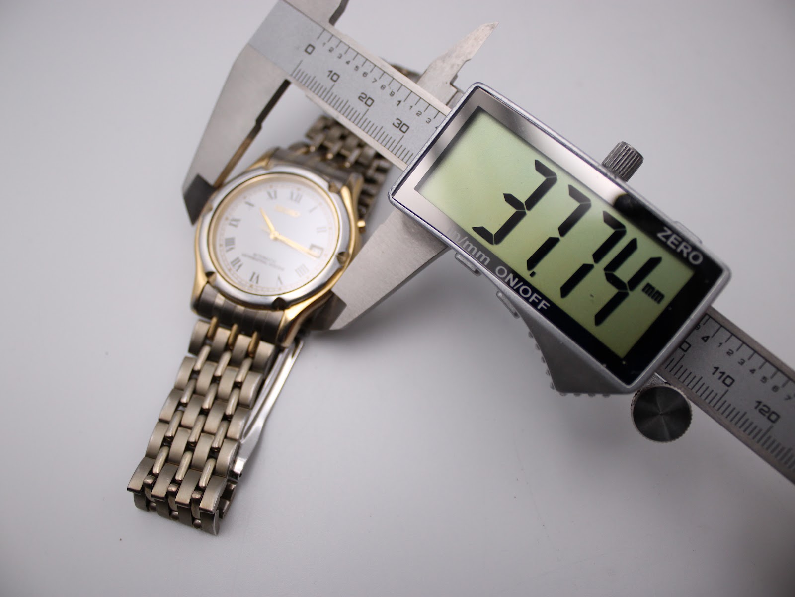 The Seiko watch being measured by a digital caliper, displaying a case diameter of 37.74mm.