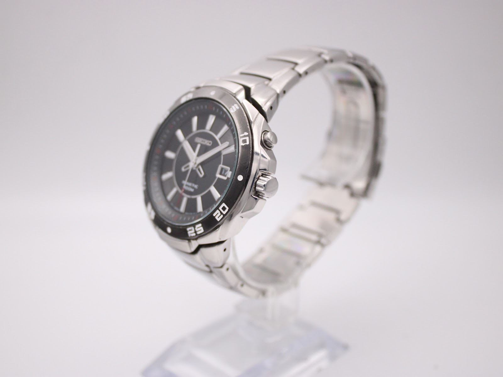 Angled view of the Seiko Kinetic watch showing the case side and integrated bracelet on a stand.