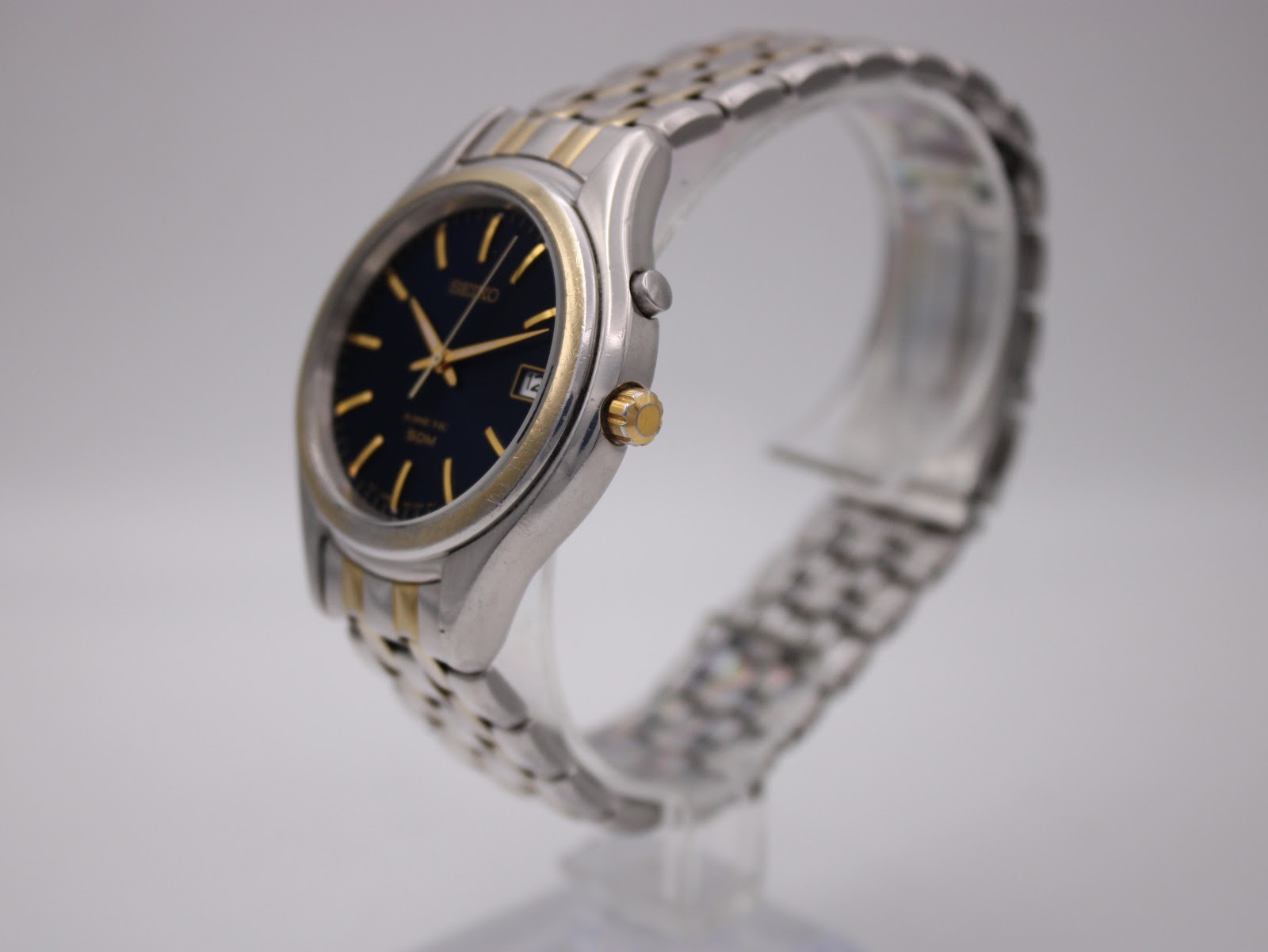 Angled side view of the Seiko Kinetic watch showing the two-tone case and bracelet on a clear display stand.