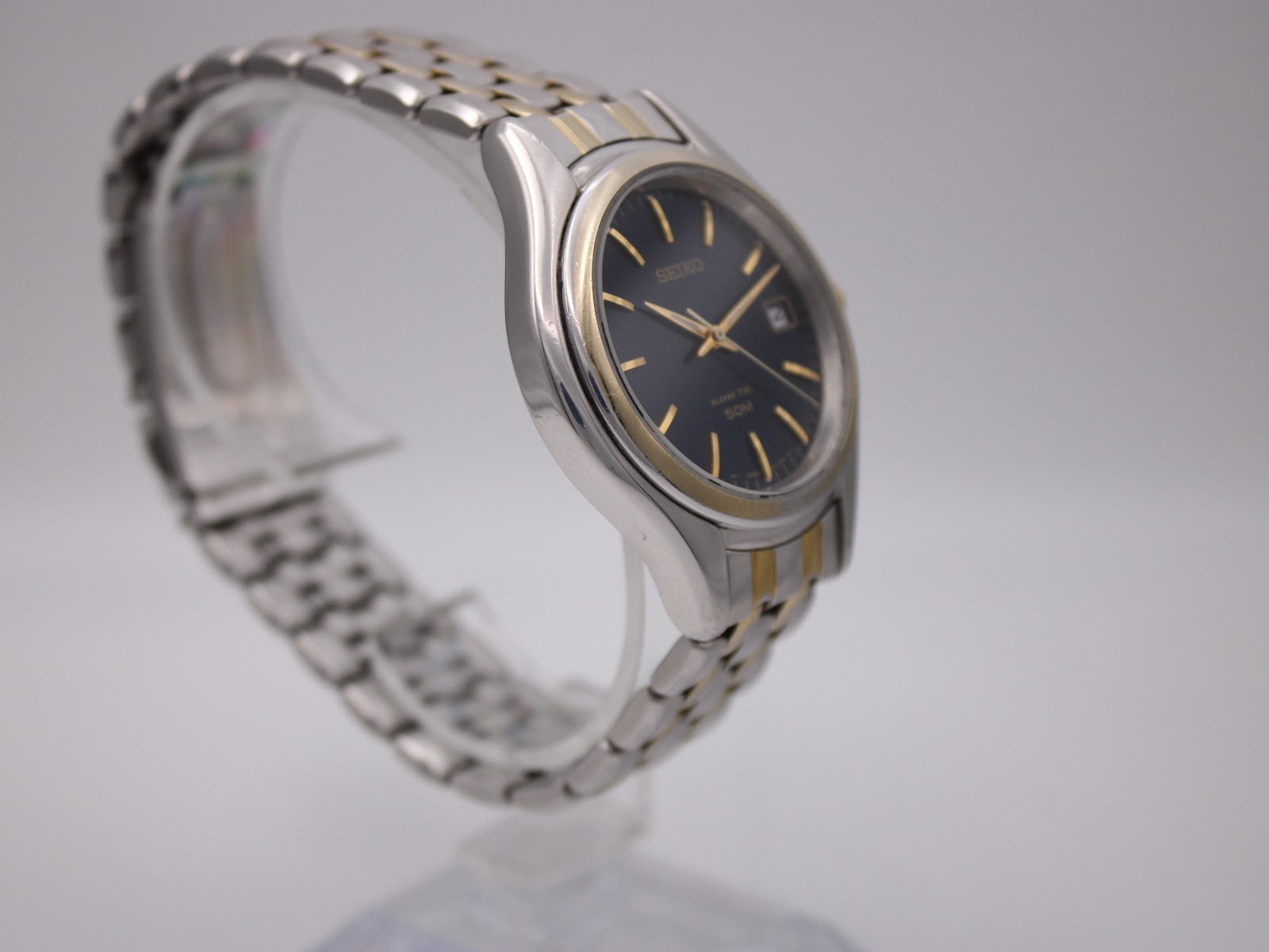 Angled side view from the other side of the Seiko Kinetic watch, highlighting the gold-tone crown and pusher.